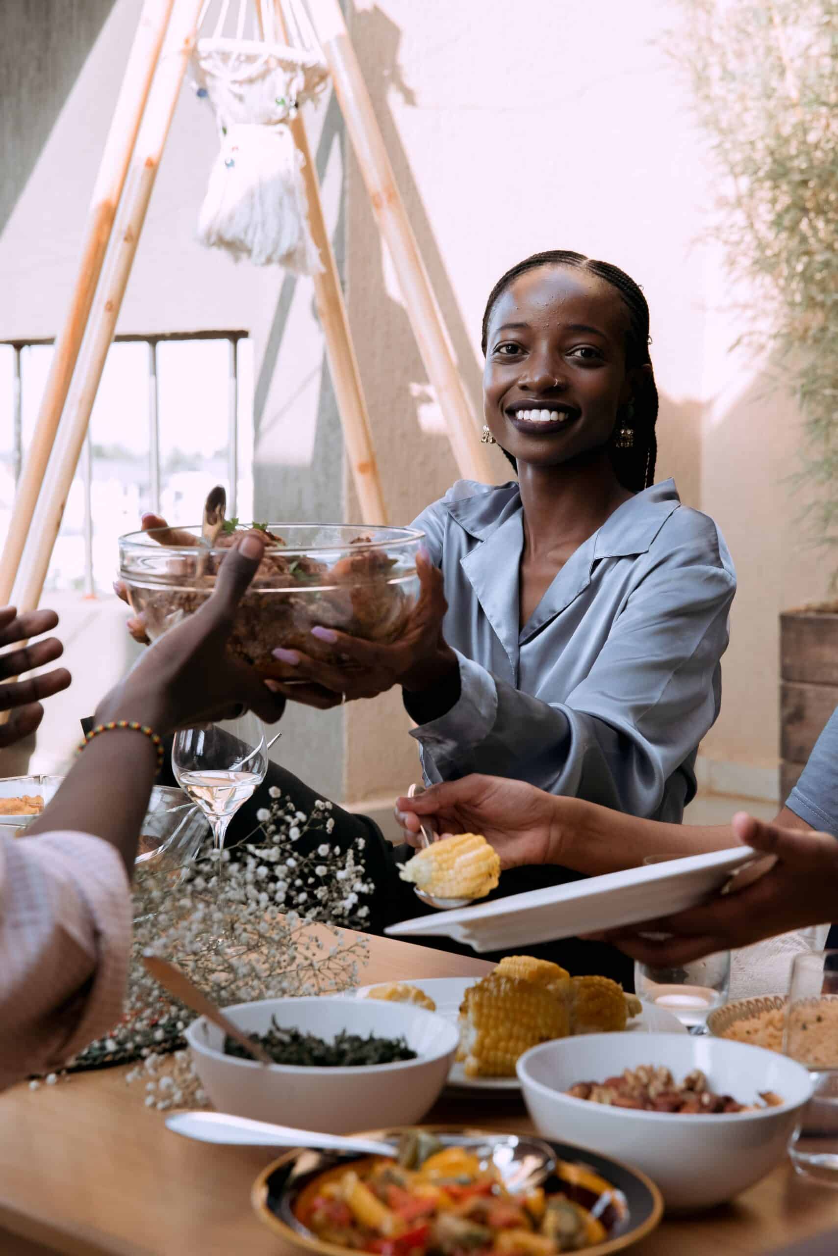 Smiling woman passing a bowl of food across the table at a shared meal