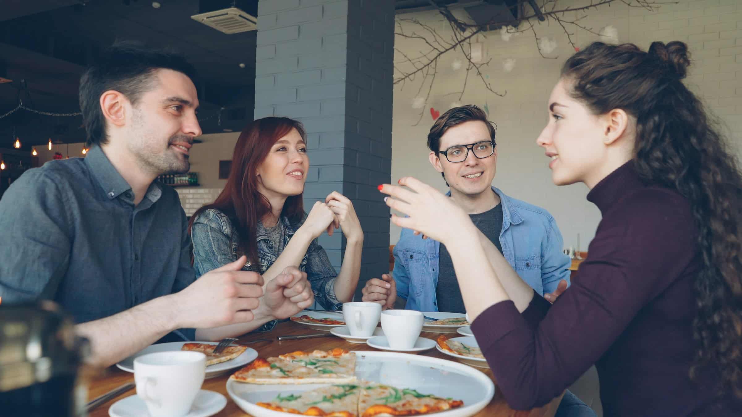 Four friends talking and laughing over pizza and coffee at a cafe table
